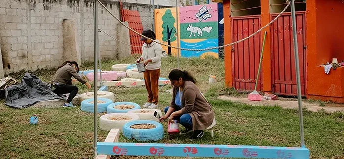 Personas colocan piezas de madera sobre un muro blanco junto a una madre con su bebé