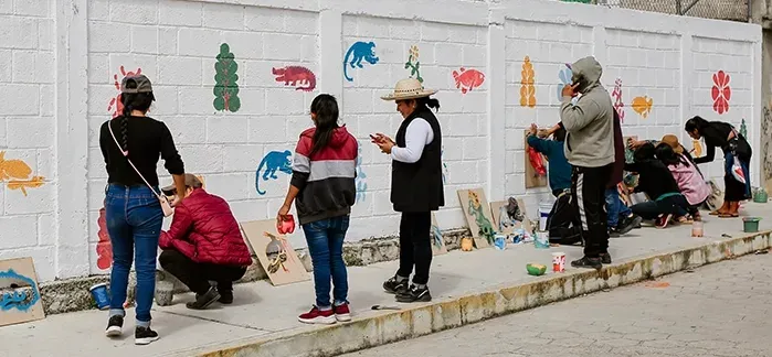 Voluntarios pintan y colocan esténciles a lo largo de un muro exterior