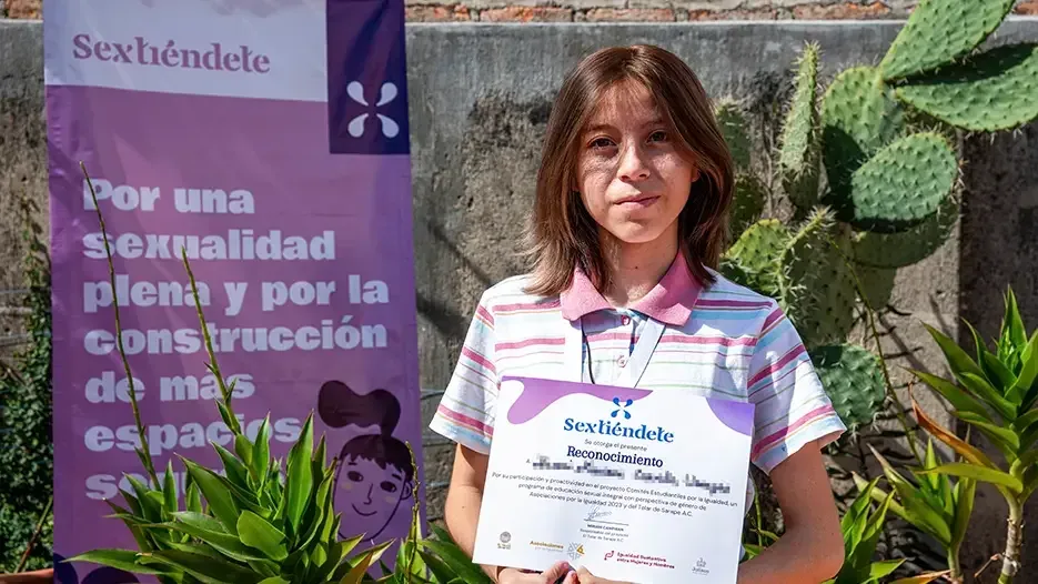 Estudiante de cabello largo muestra su reconocimiento entre plantas y la lona del programa