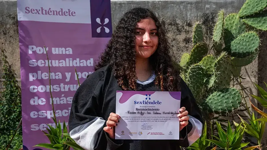 Estudiante de cabello rizado con toga sostiene su reconocimiento del programa