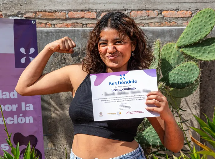 Joven sonríe mientras muestra un reconocimiento de participación