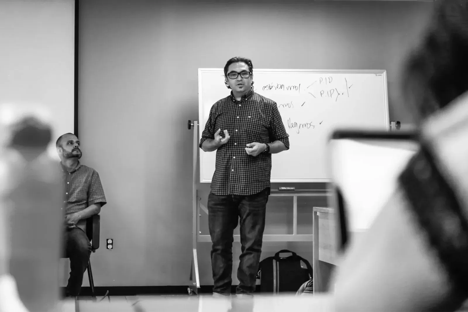 Facilitador explica frente a un pizarrón en una sala de taller, en blanco y negro