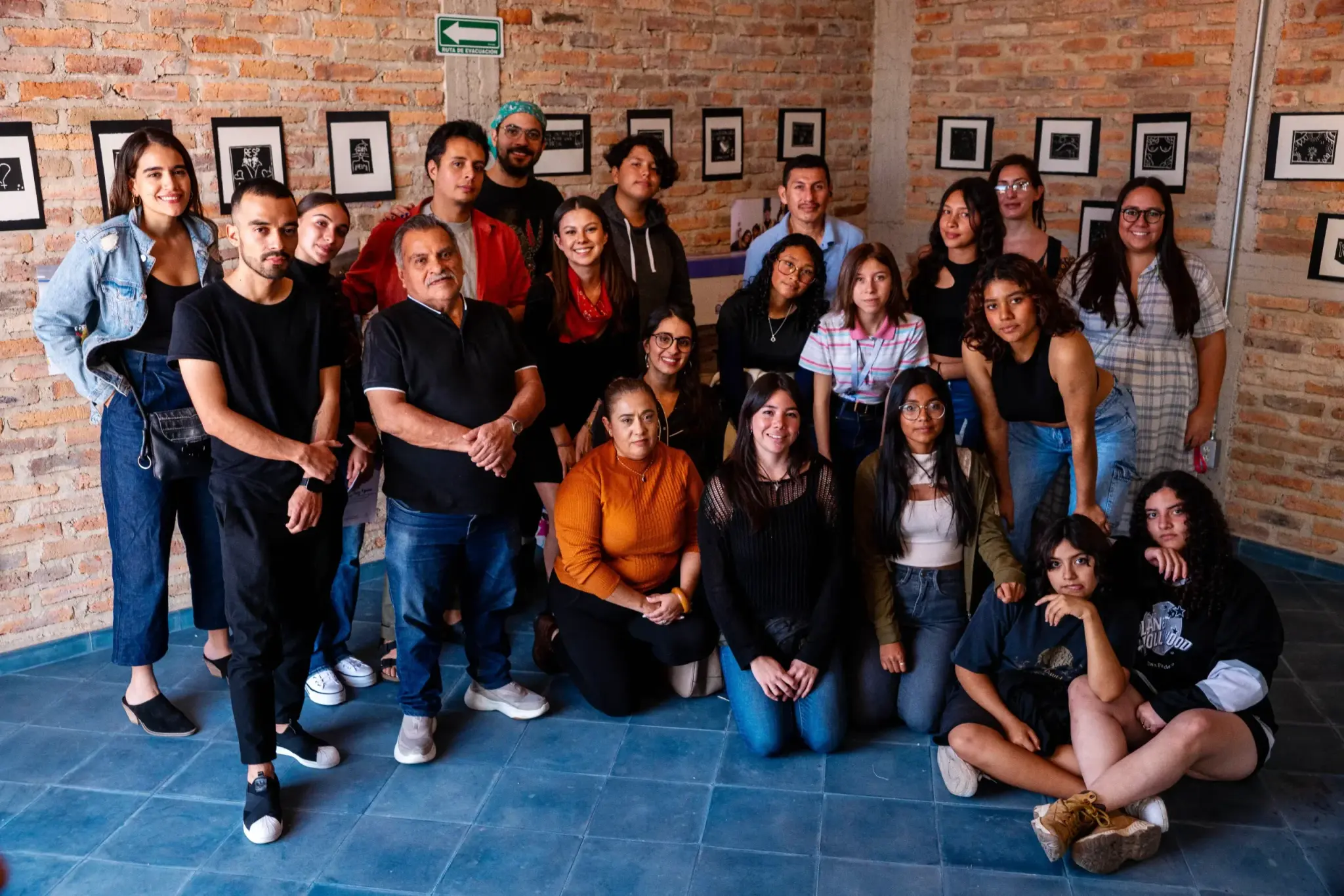 Grupo de estudiantes y talleristas posa de pie y sentado en un patio con muro de ladrillo