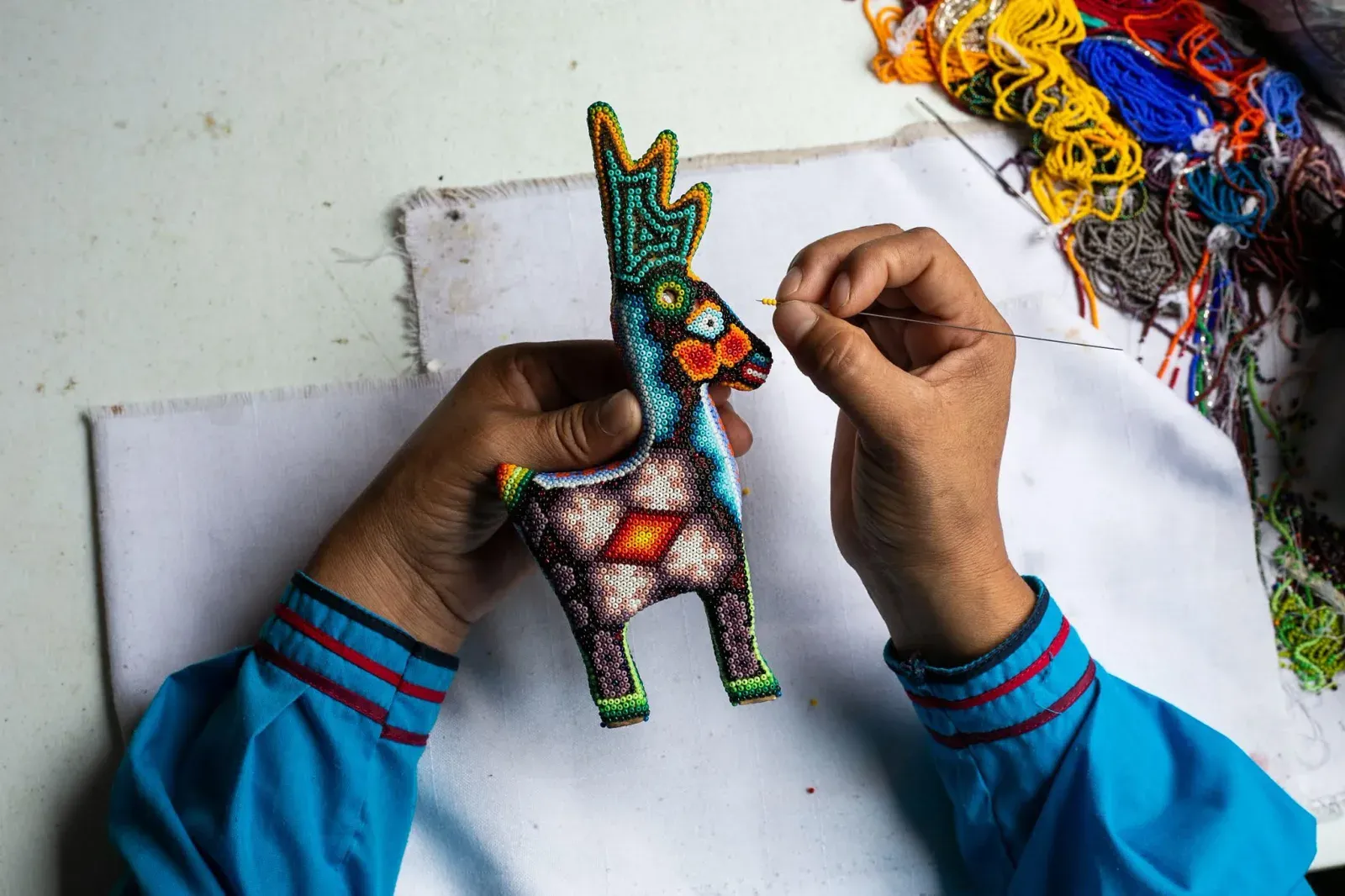 Manos decoran con chaquira de colores una figura de animal tallada en madera